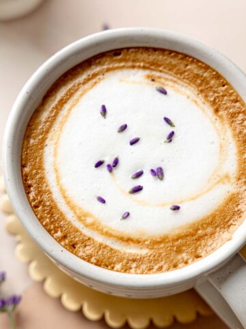 A lavender latte topped with foamy milk and sprinkled with dried lavender buds.