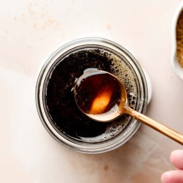 Spoon dipping into a jar of dark liquid cane sugar syrup.