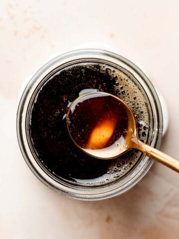 Spoon dipping into a jar of dark liquid cane sugar syrup.